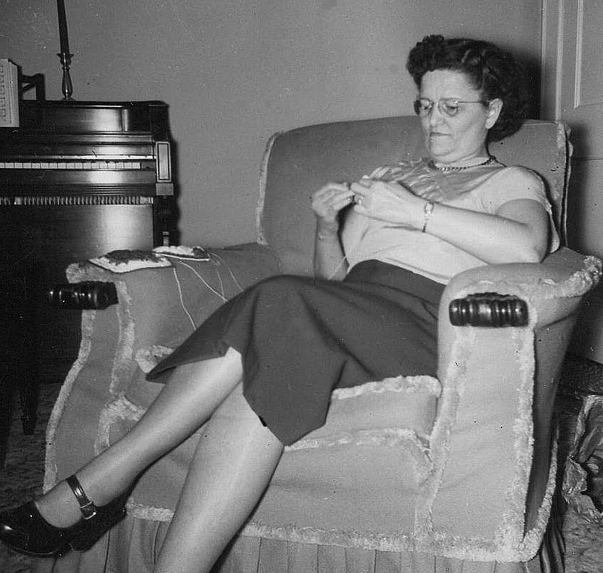 Louise Wingate Beard in an armchair crocheting, a piano behind her